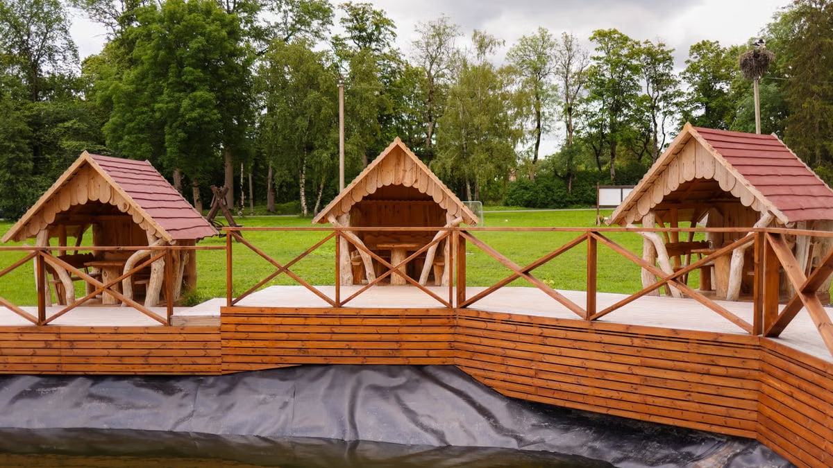 Rustic wooden gazebos overlooking a peaceful pond surrounded by lush green trees.